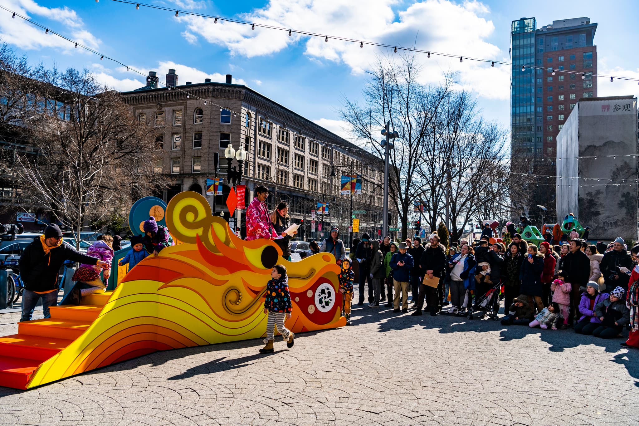 People surround a bright yellow, orange, and red dragon sculpture in Chinatown, Boston.